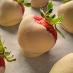 white chocolate covered strawberries on a parchment lined baking sheet