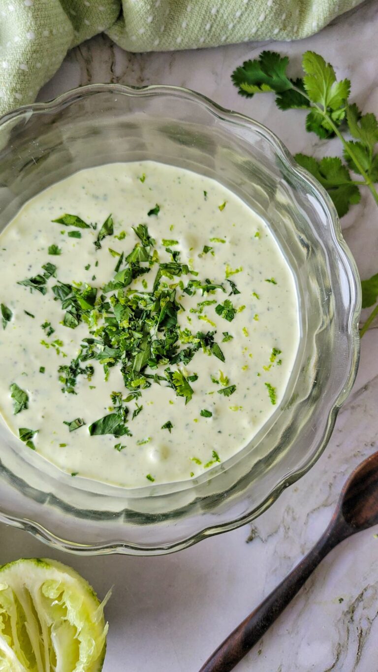 cilantro lime crema topped with chopped cilantro in a glass bowl, next to a spoon, wedge of lime, and more cilantro.