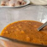 orange sauce in a bowl, plate of raw chicken thighs in the background