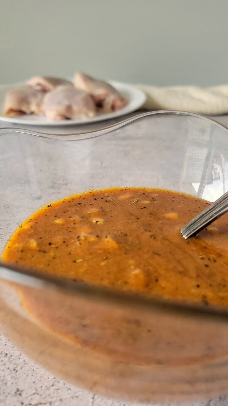 orange sauce in a bowl, plate of raw chicken thighs in the background