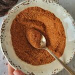 hand holding a bowl of bbq dry rub, spoon in the bowl