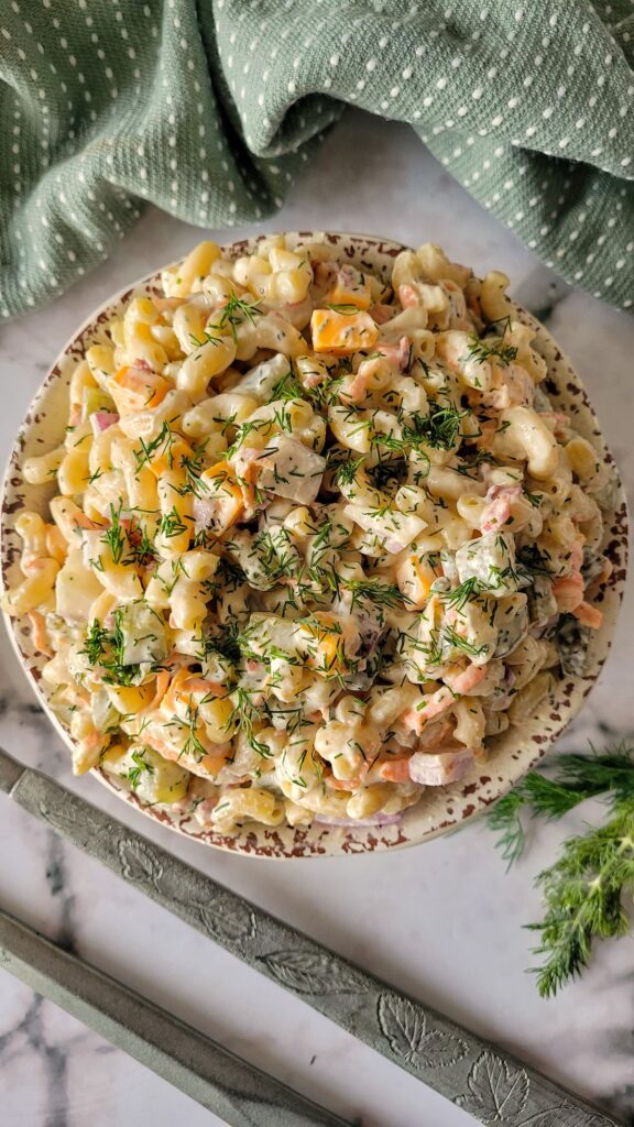 bowl of creamy pasta salad with chopped cheese, pickles, dill, onions
