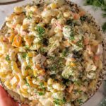 hand holding a bowl of dill pickle pasta salad with chopped fresh dill, pickles, cubed cheddar cheese, and onions