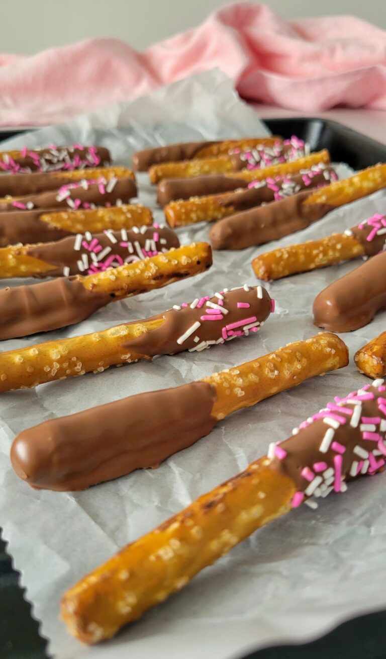 milk chocolate covered pretzel rods with sprinkles on a parchment lined baking sheet
