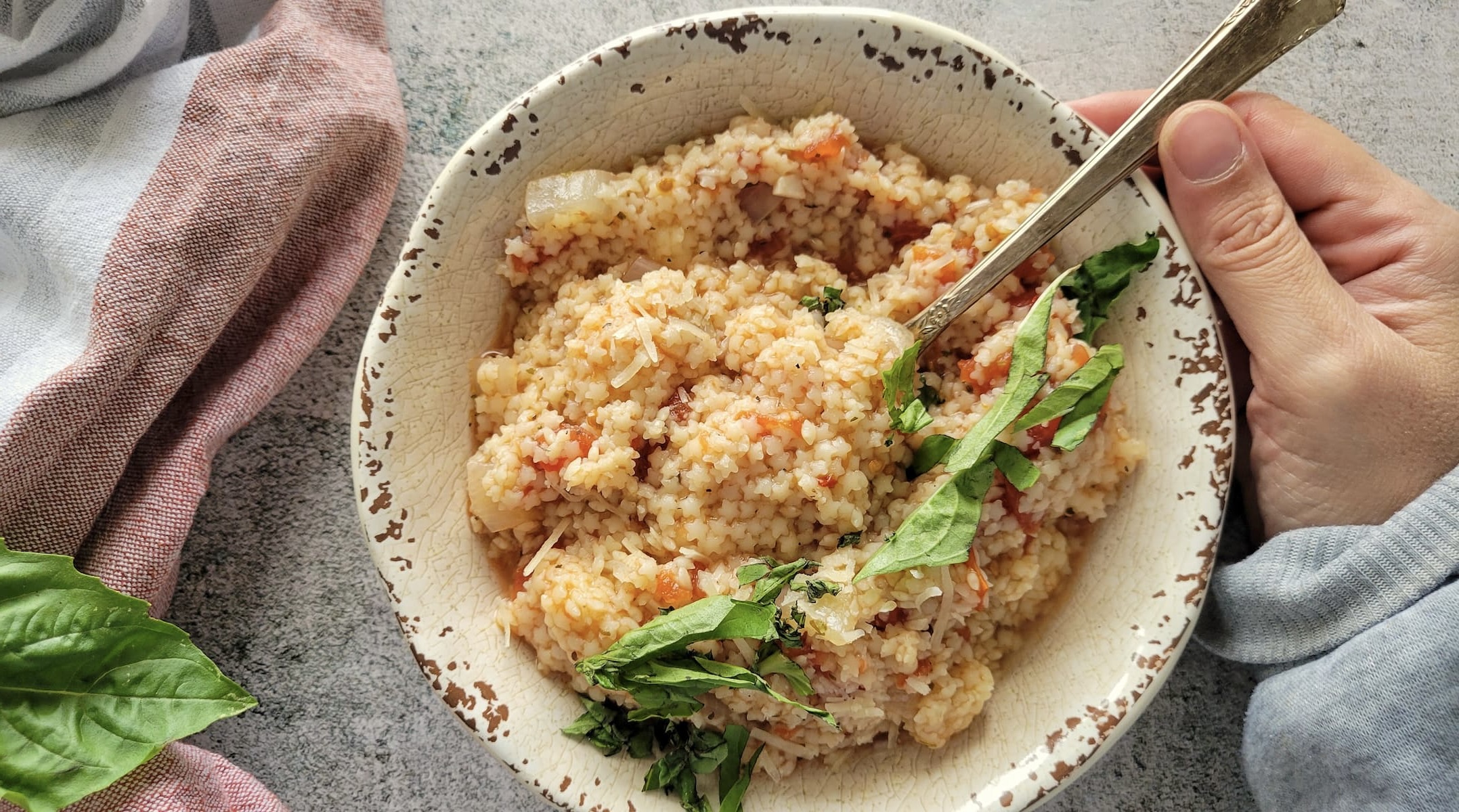 hand holding a bowl of tomato pastina with fresh basil