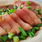 tuna sashimi on a plate with green onions and soy sauce