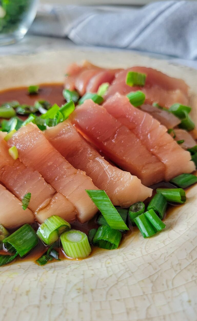 tuna sashimi on a plate with green onions and soy sauce