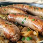 5 cooked sausages in a skillet on a bed of cabbage with fresh parsley