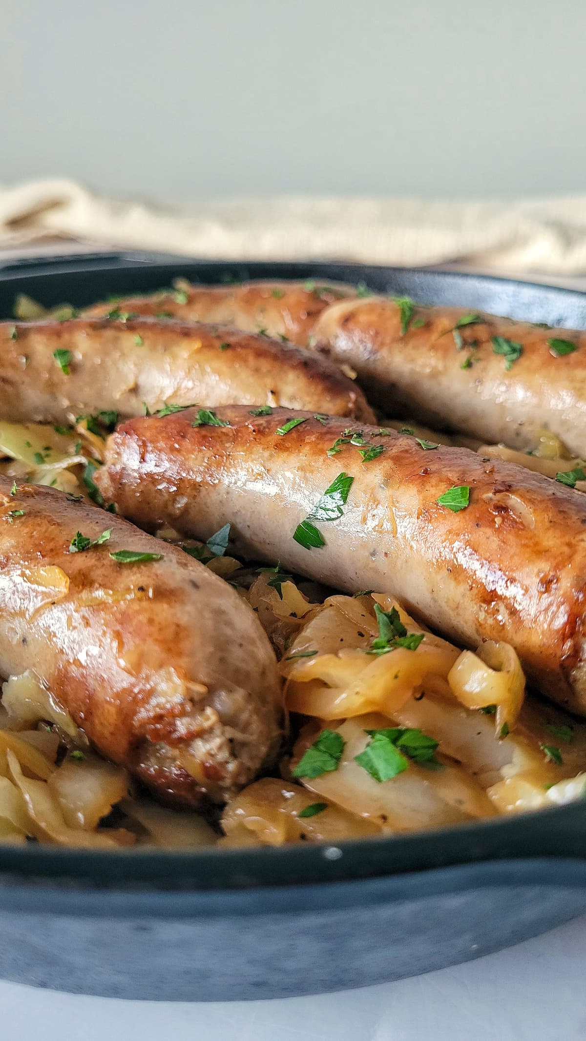 5 cooked sausages in a skillet on a bed of cabbage with fresh parsley