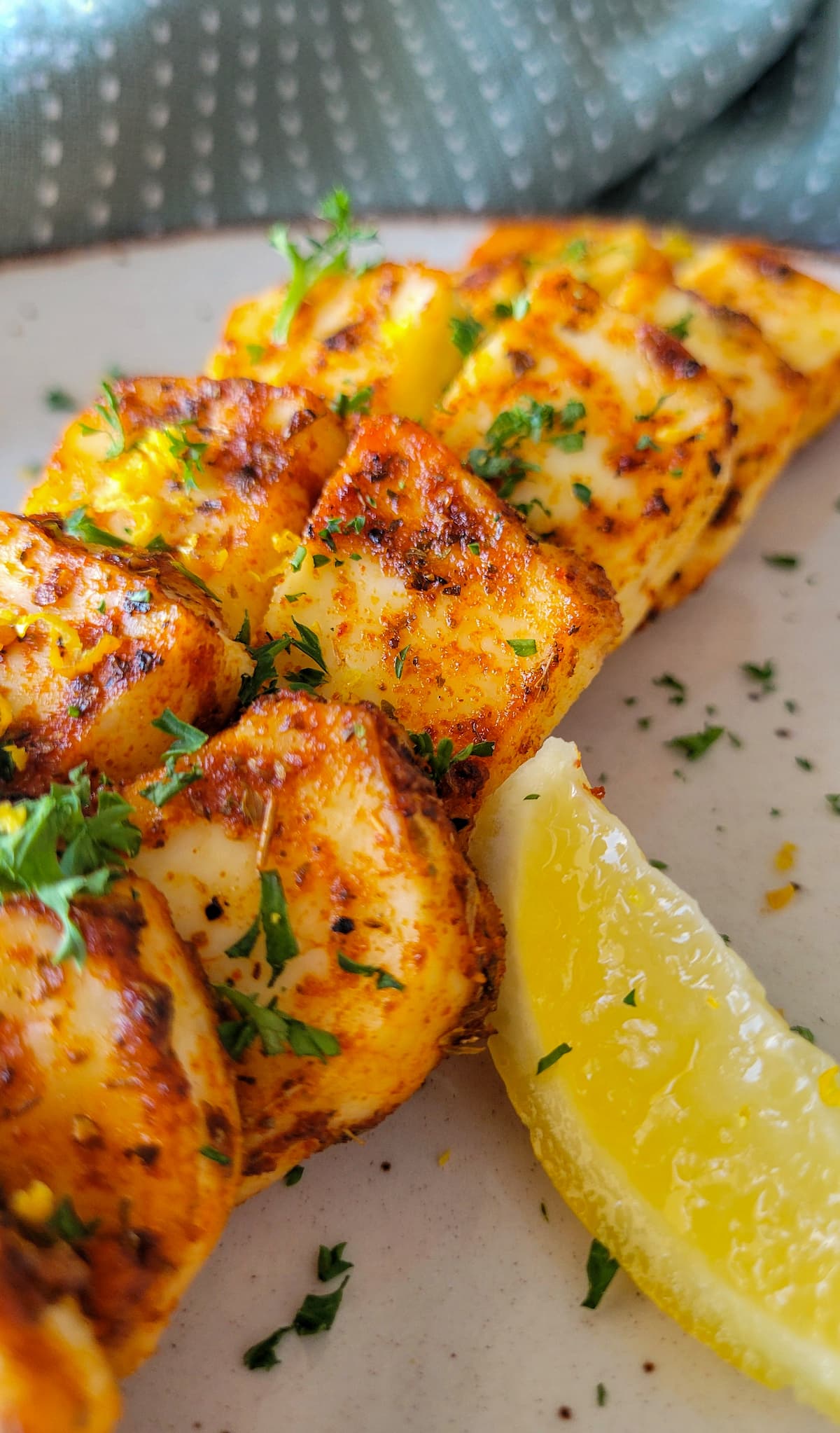 crispy halloumi cheese sliced up on a plate with a lemon wedge and fresh parsley
