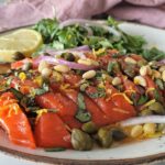 salmon crudo on a plate with sliced red onions, pine nuts, capers, basil, lemon zest, lemon, and arugula