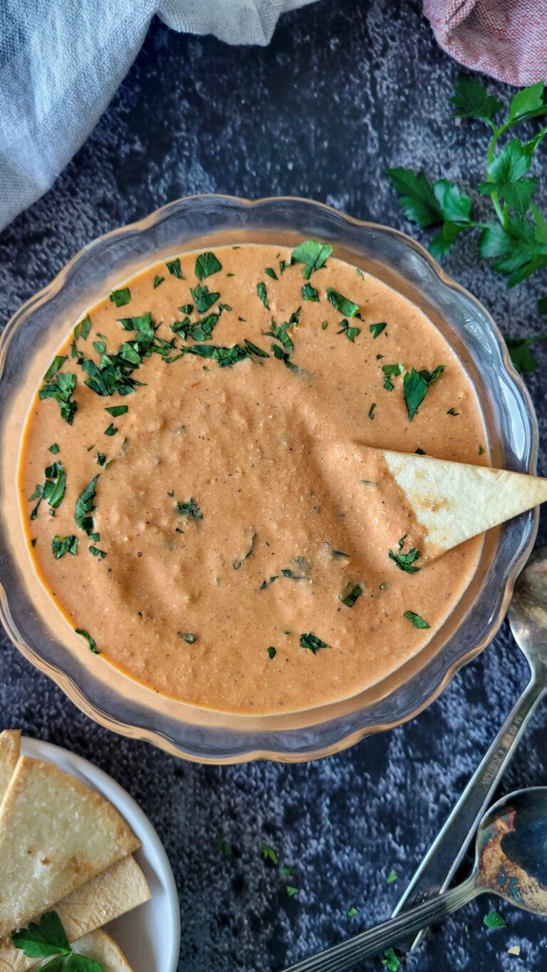 orange queso dip with cilantro in a bowl with a triangular pita