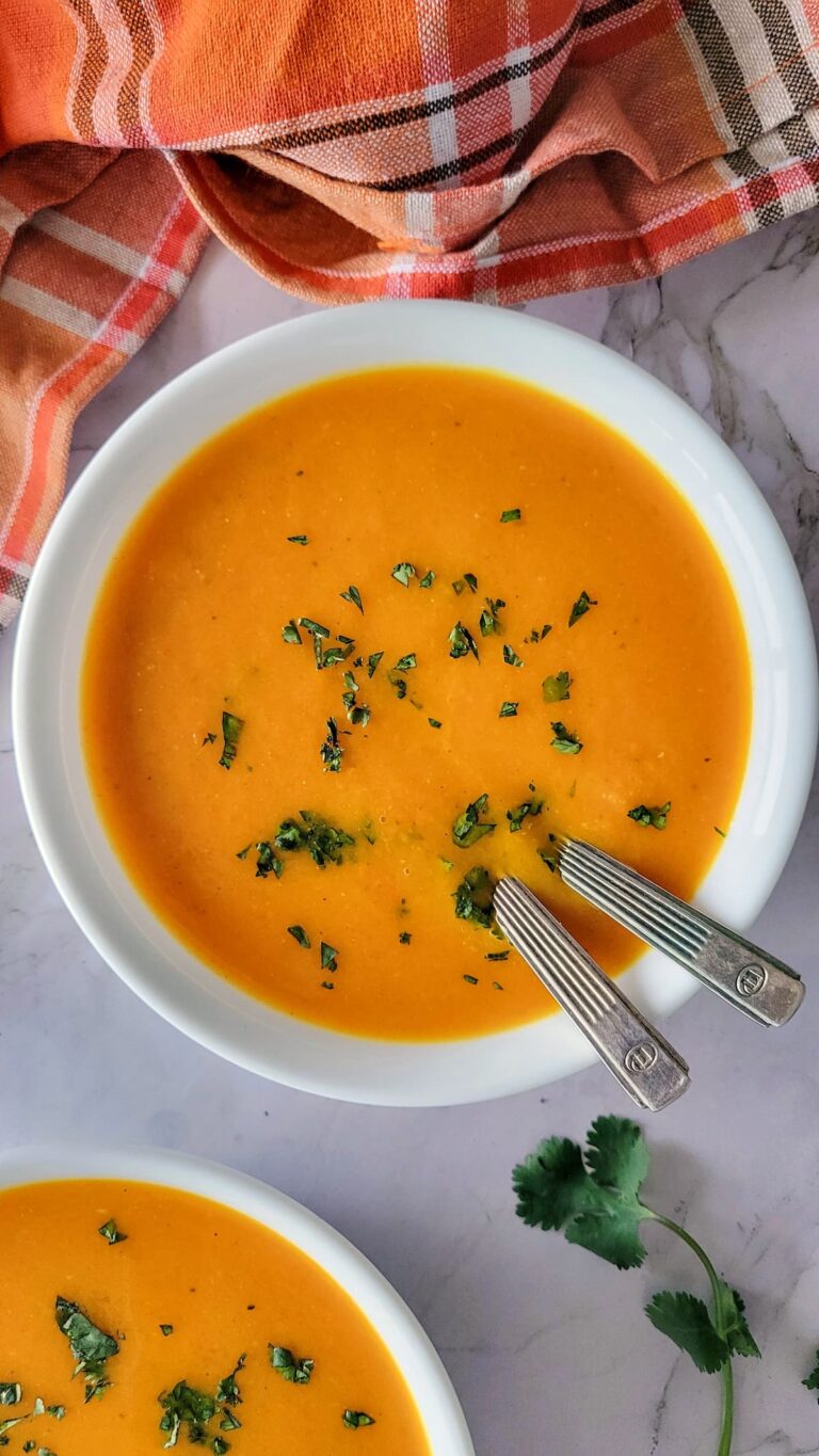 two bowls of orange soup with chopped parsley on top