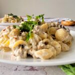 plate of creamy sausage pasta with fresh basil on top, another plate in the background