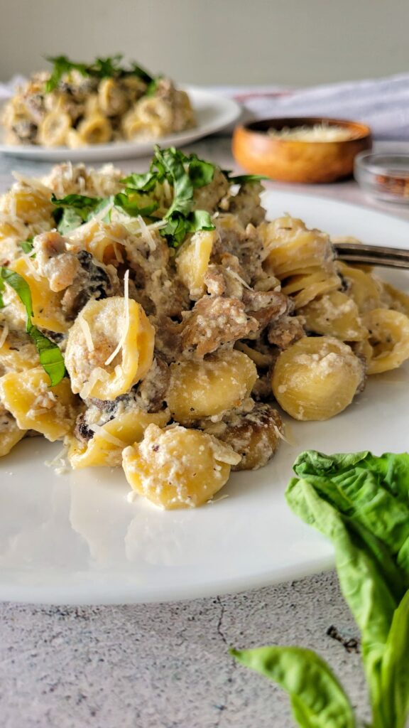 creamy pasta and sausage on a plate with fresh chopped basil and parmesan cheese