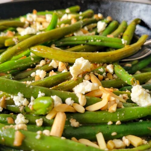cooked green beans in a skillet with feta and almonds