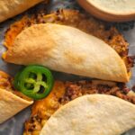 cheesy ground beef tacos on a parchment lined tray with sliced jalapenos