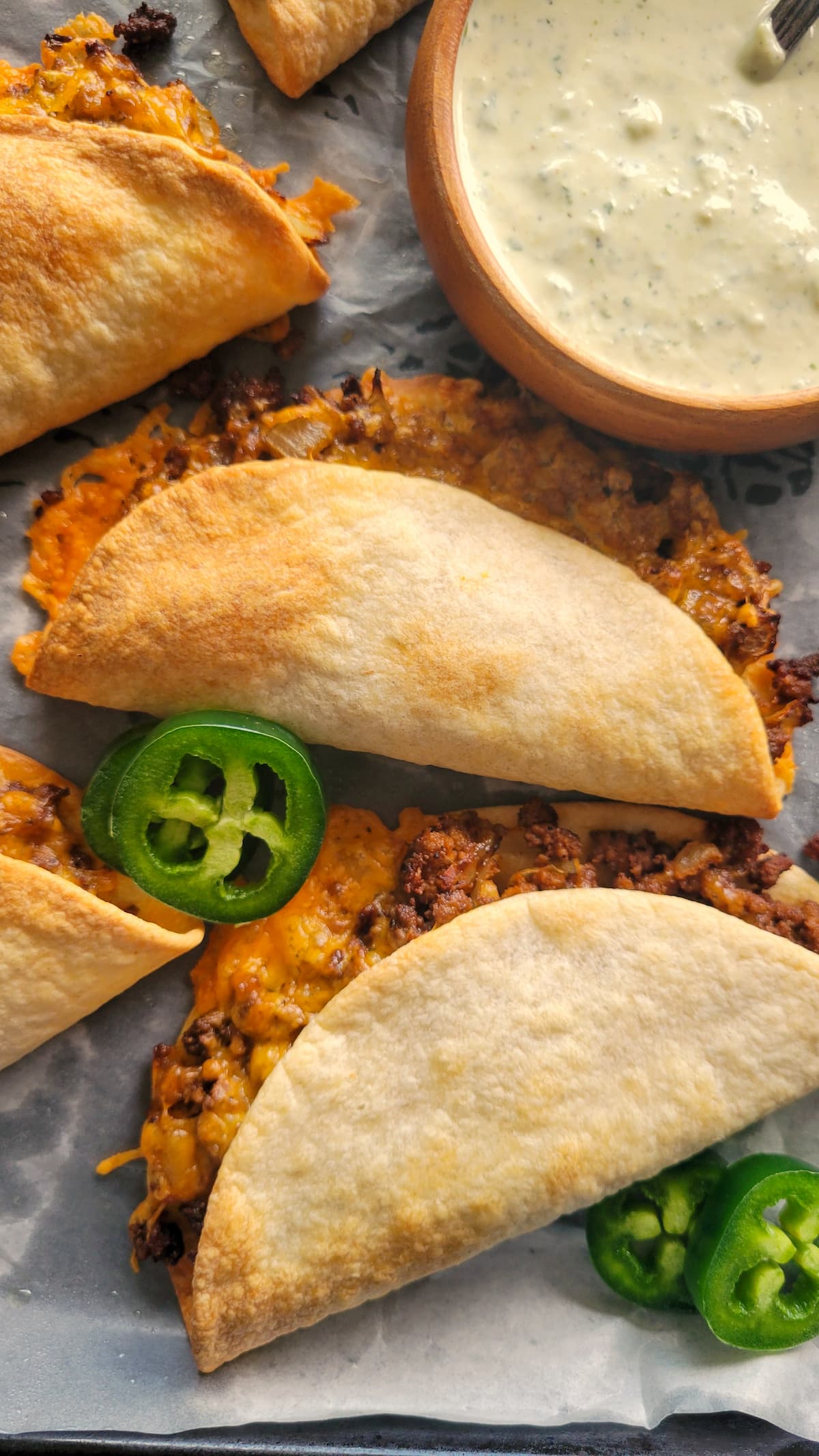 cheesy ground beef tacos on a parchment lined tray with sliced jalapenos