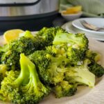 broccoli piled on a plate with lemon, instant pot in the background