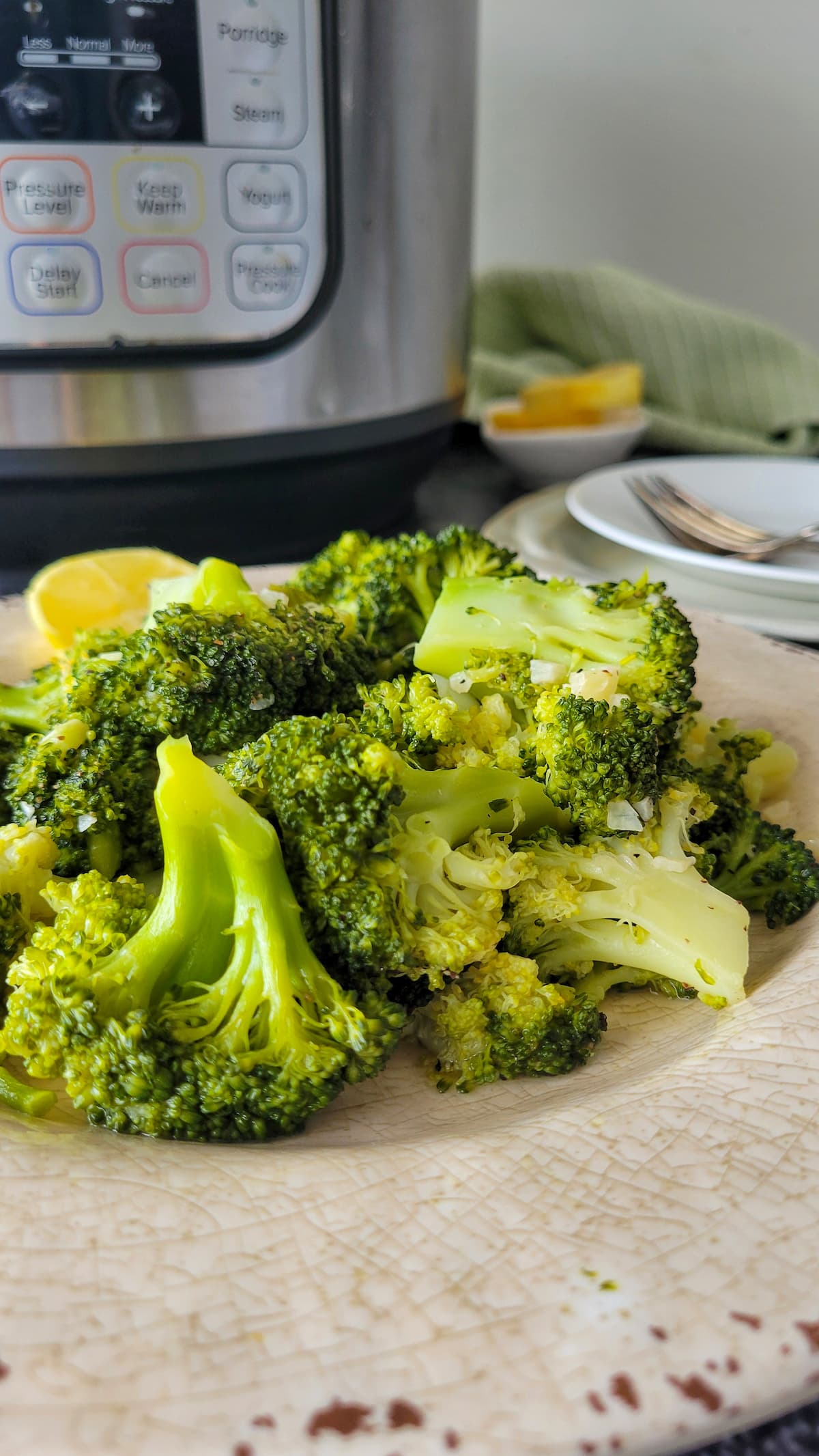 broccoli piled on a plate with lemon, instant pot in the background