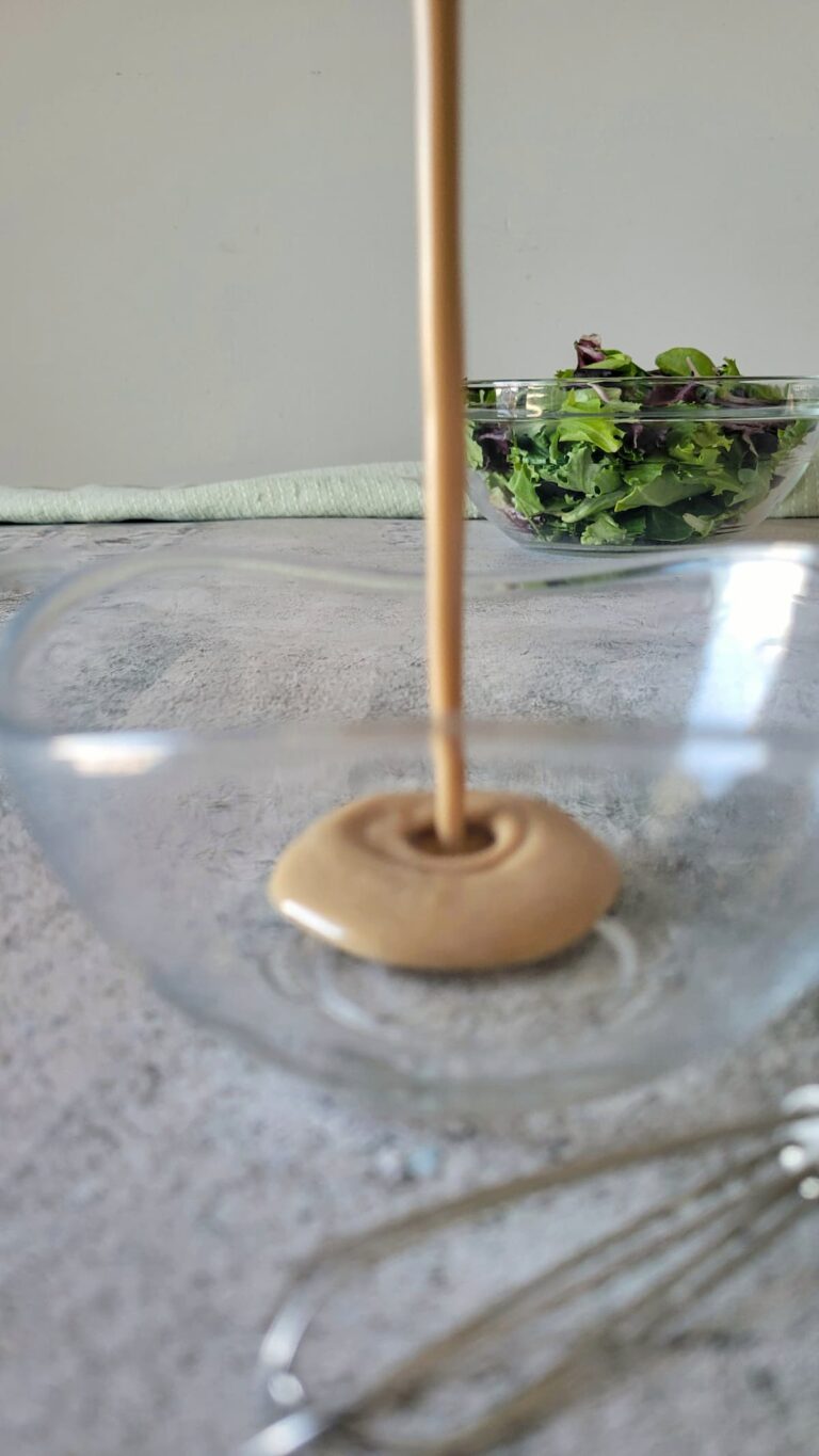 creamy balsamic dressing pouring into a bowl, bowl of lettuce in the background