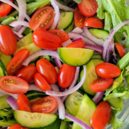 bowl of mixed greens topped with halved cherry tomatoes, sliced red onions, and diced cucumbers