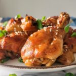 glazed chicken drumsticks on a plate with sesame seeds and green onions