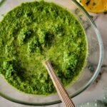sauce with parsley in a bowl with a spoon, garlic and lemon in the background