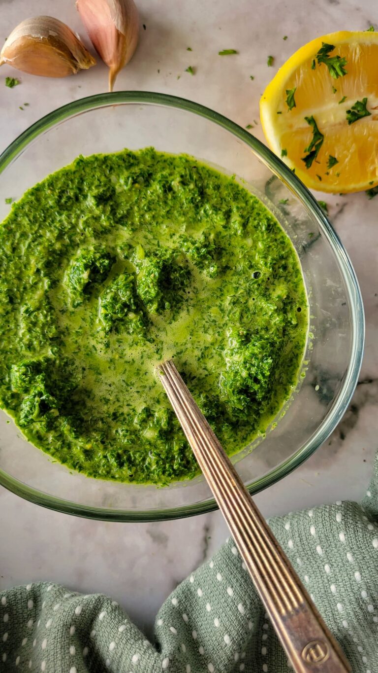 sauce with parsley in a bowl with a spoon, garlic and lemon in the background