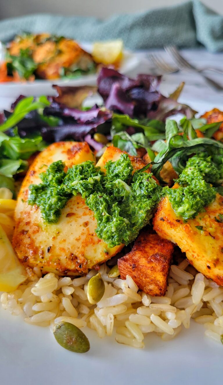 halloumi cheese with parsley sauce on a plate with sweet potatoes, rice, and greens