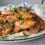 smashed crispy potatoes piled on a plate on top of a creamy orange sauce, topped with fresh chopped chives