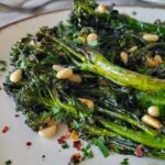 a pile of roasted broccolini on a plate with toasted pine nuts and chili flakes
