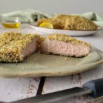 thick breaded pork chop on a plate, cut in half, fork and knife in the front, more chops in the background