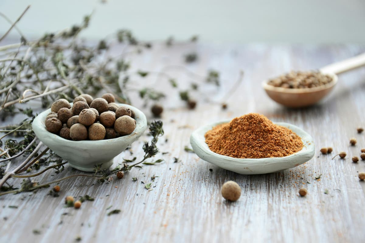 bowl of whole allspice next to bowl of ground