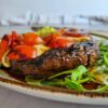 portobello mushroom stuffed with cherry tomatoes and bocconcini cheese on arugula on a plate