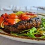 portobello mushroom stuffed with cherry tomatoes and bocconcini cheese on arugula on a plate
