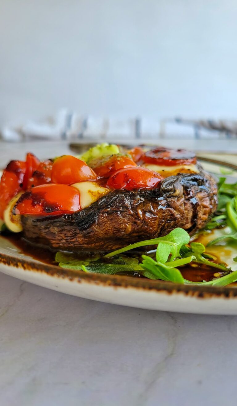 portobello mushroom stuffed with cherry tomatoes and bocconcini cheese on arugula on a plate