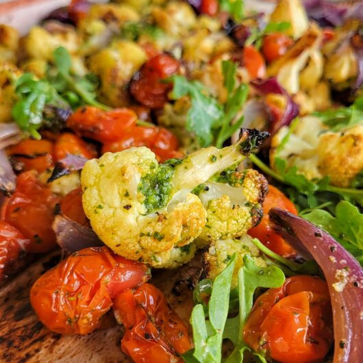 cauliflower with pesto, red onions, arugula, cherry tomatoes, and lemon on a sheet pan