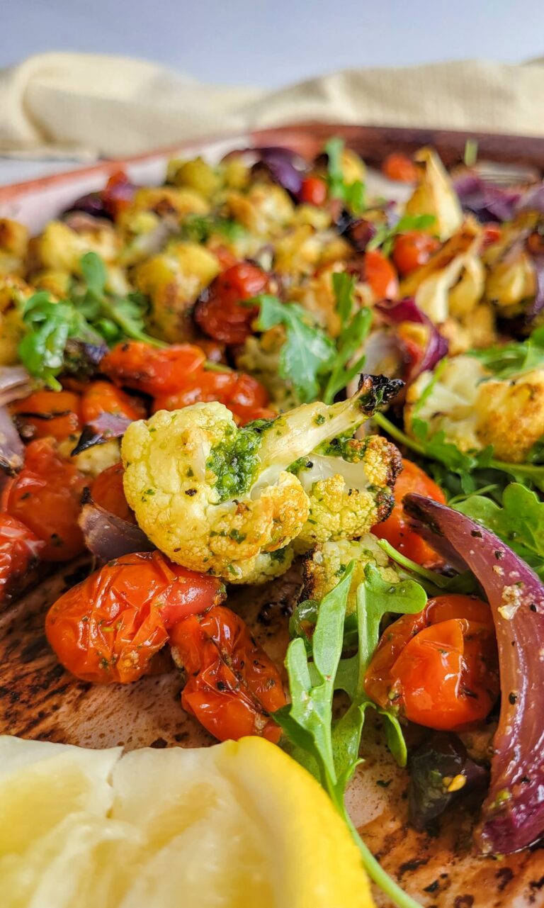 cauliflower with pesto, red onions, arugula, cherry tomatoes, and lemon on a sheet pan