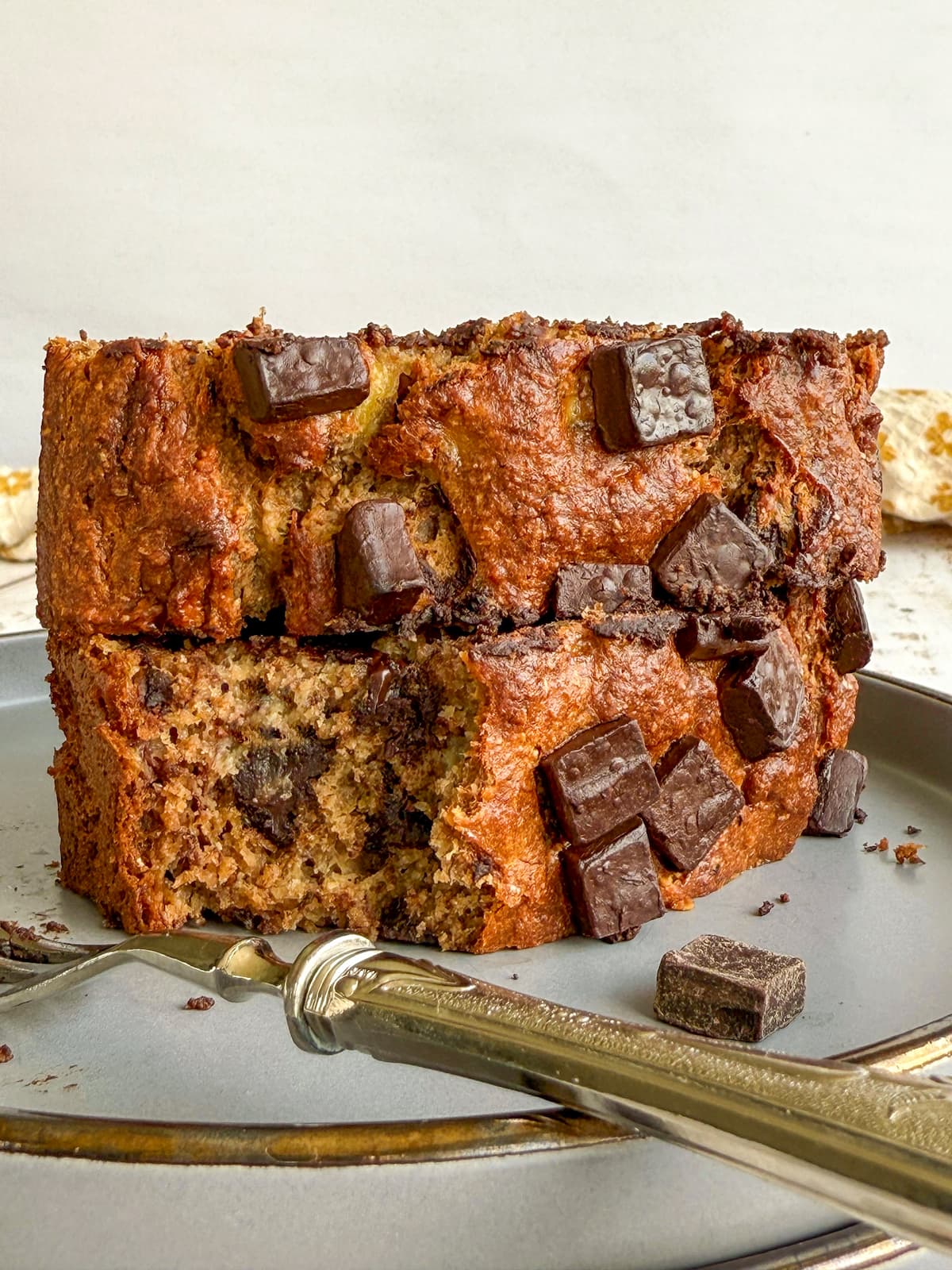 2 pieces of chocolate chunk banana bread stacked on a plate with a fork, bite missing from one