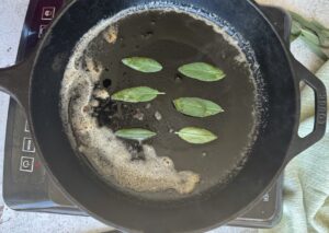 6 sage leaves frying in butter in a cast iron skillet