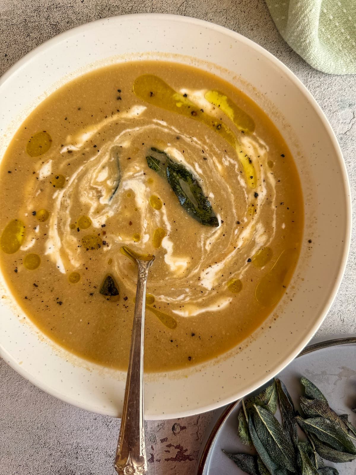 sour cream swirled into a bowl of soup with olive oil, black pepper, and crispy sage leaves