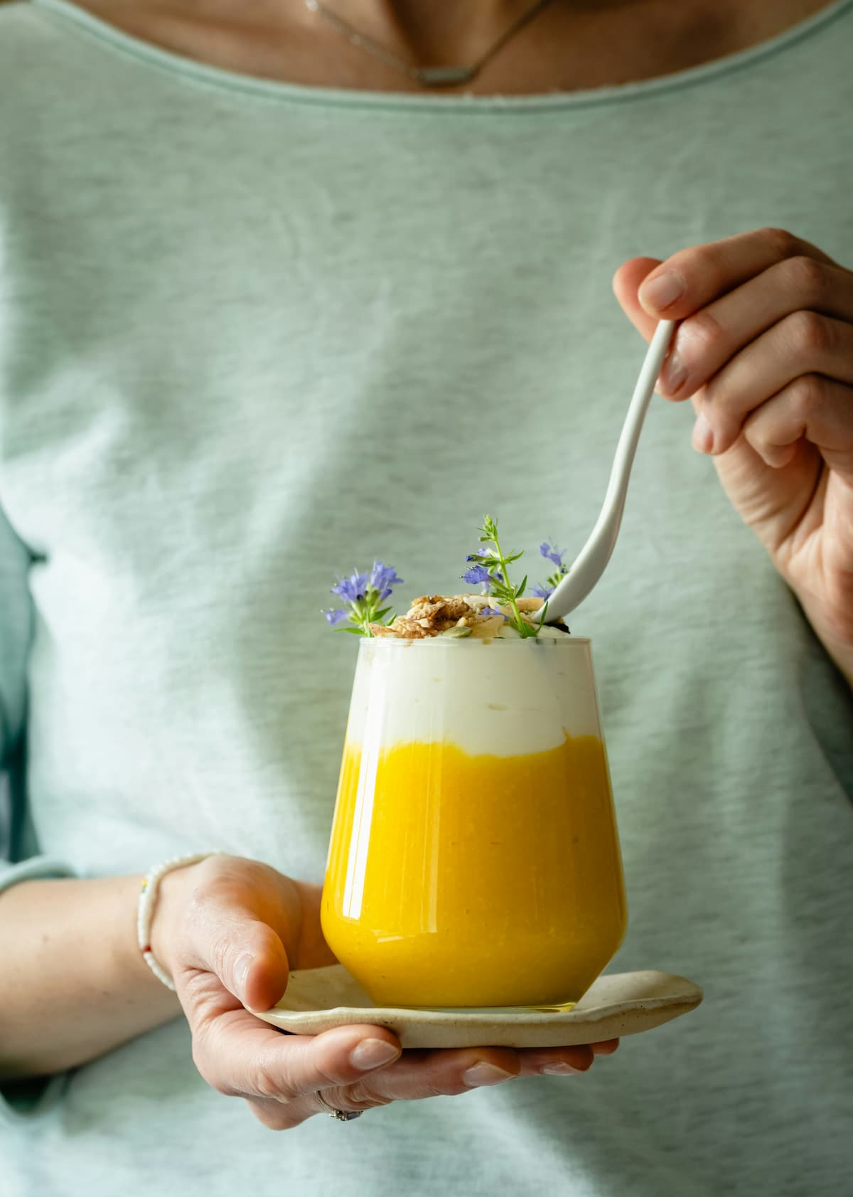 mango lassi yogurt in a cup with toppings, person with a spoon in the background