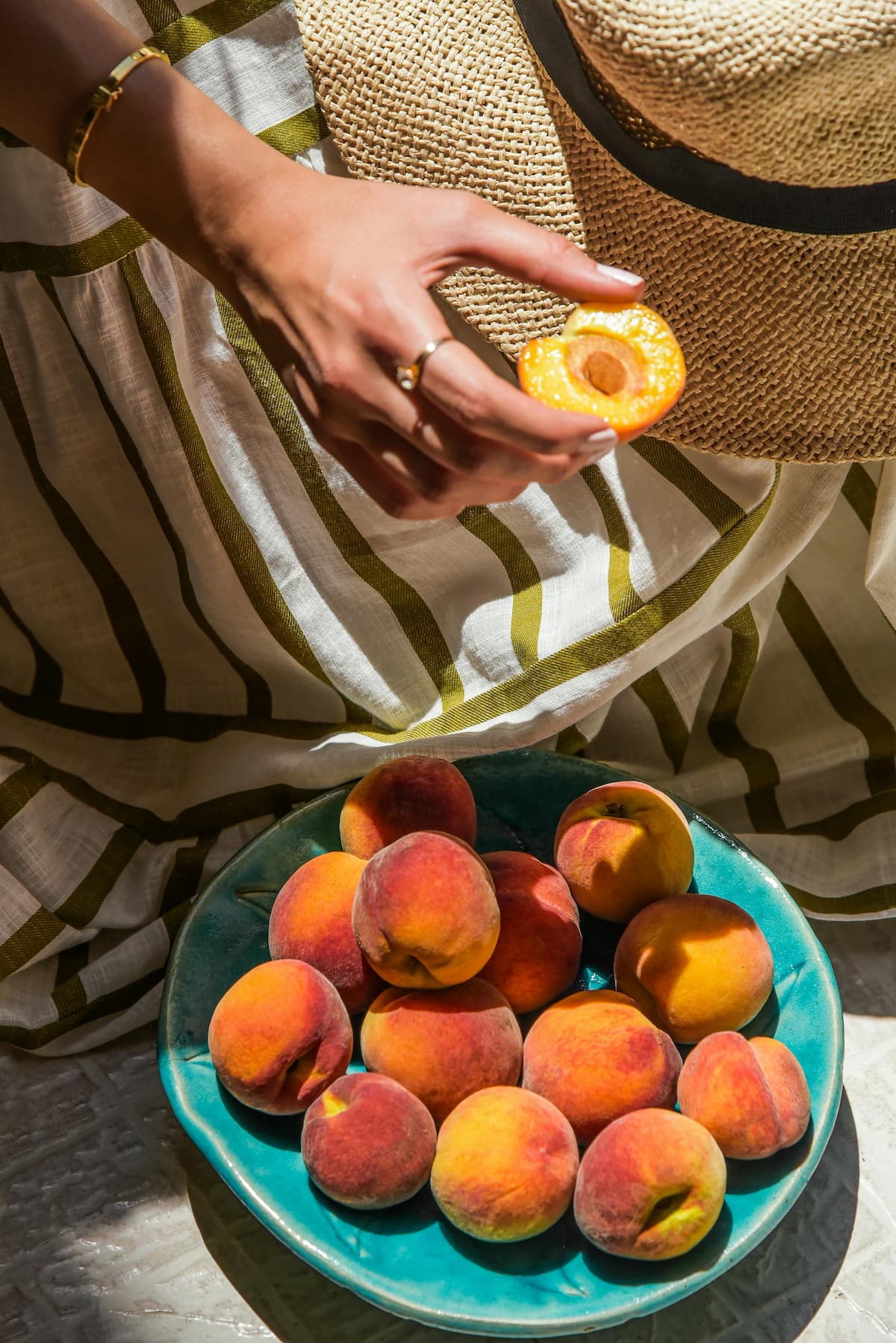 hand with a half of a peach with no pit over a plate of whole peaches