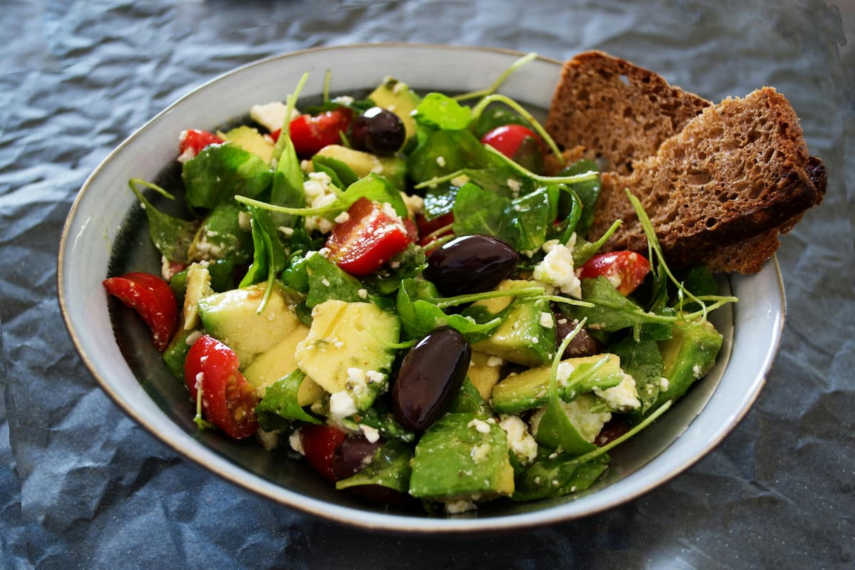 salad with avocado, kalamata olives, feta, tomatoes, sliced bread on the side
