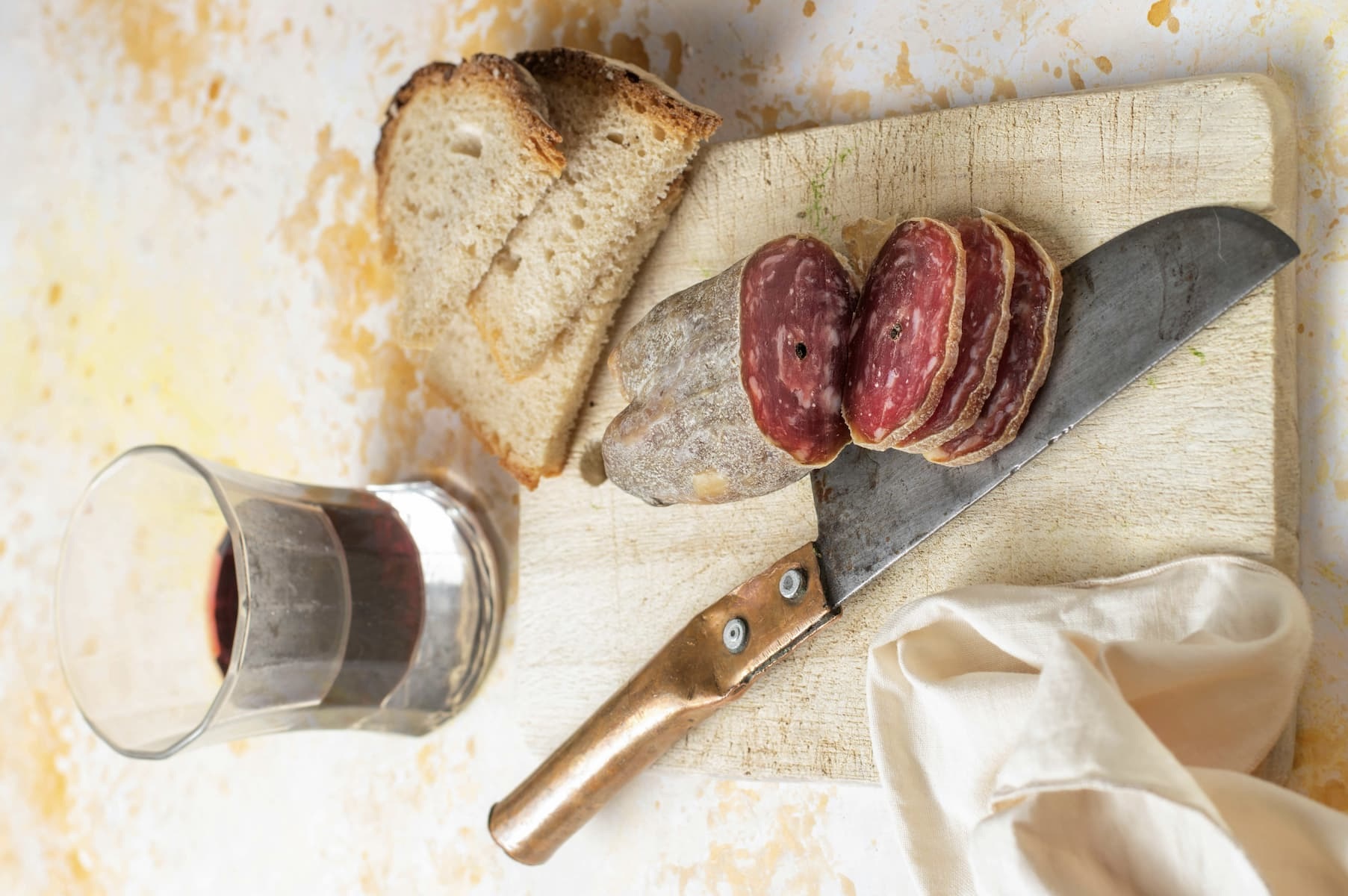 sliced hard salami on a cutting board with a knife, slices of bread, and a cup of coffee