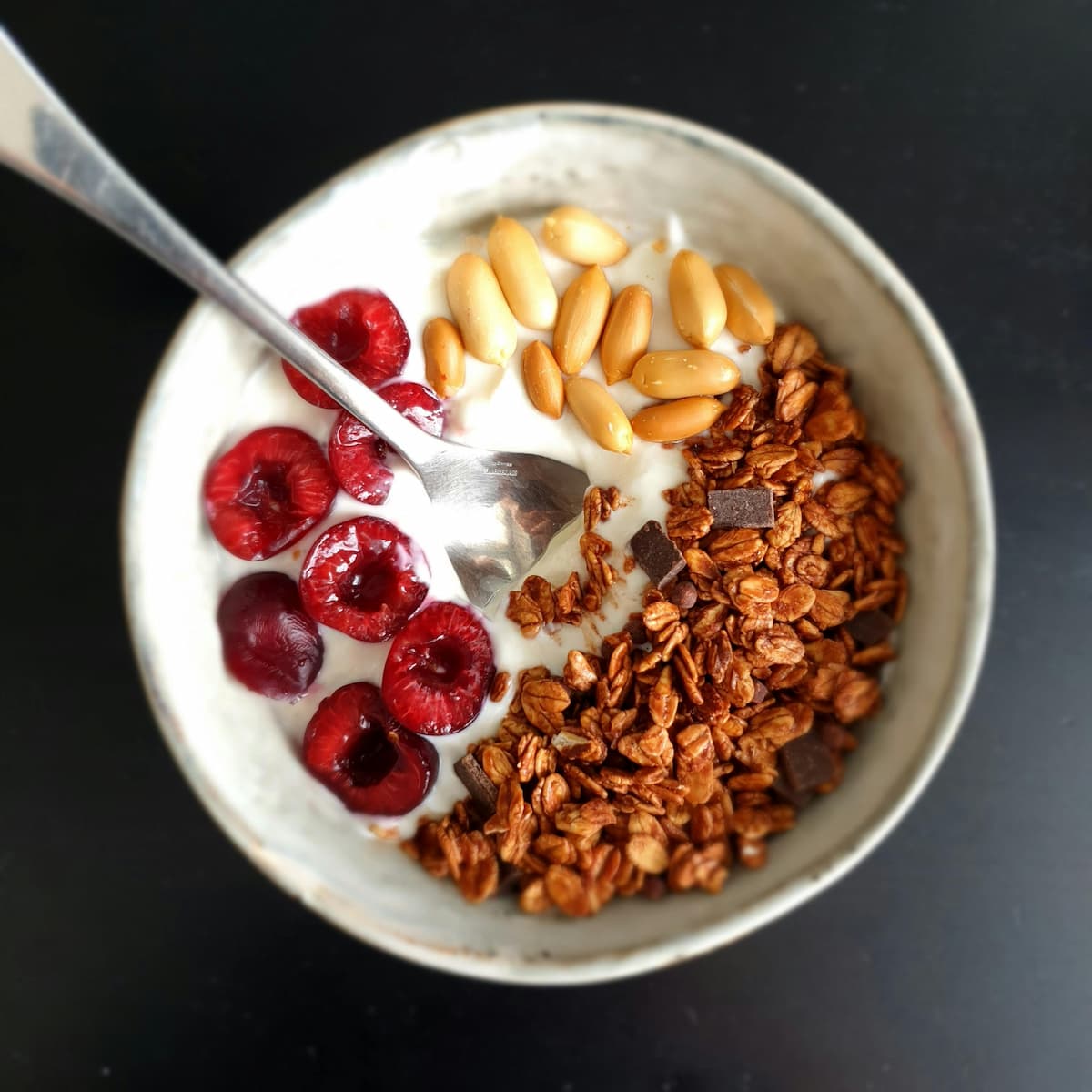 yogurt bowl with nuts, chocolate chips, granola, and halved cherries