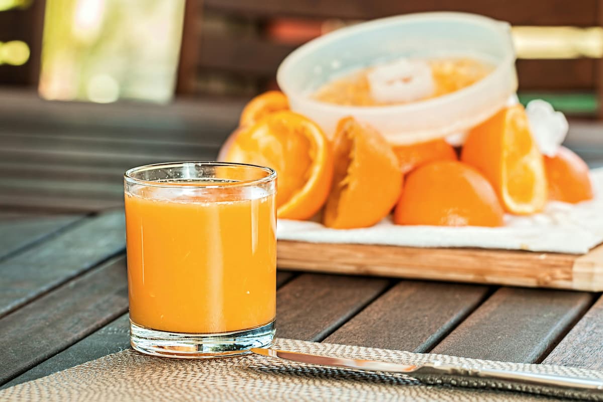 juicer with juiced oranges behind a glass of freshly squeezed orange juice