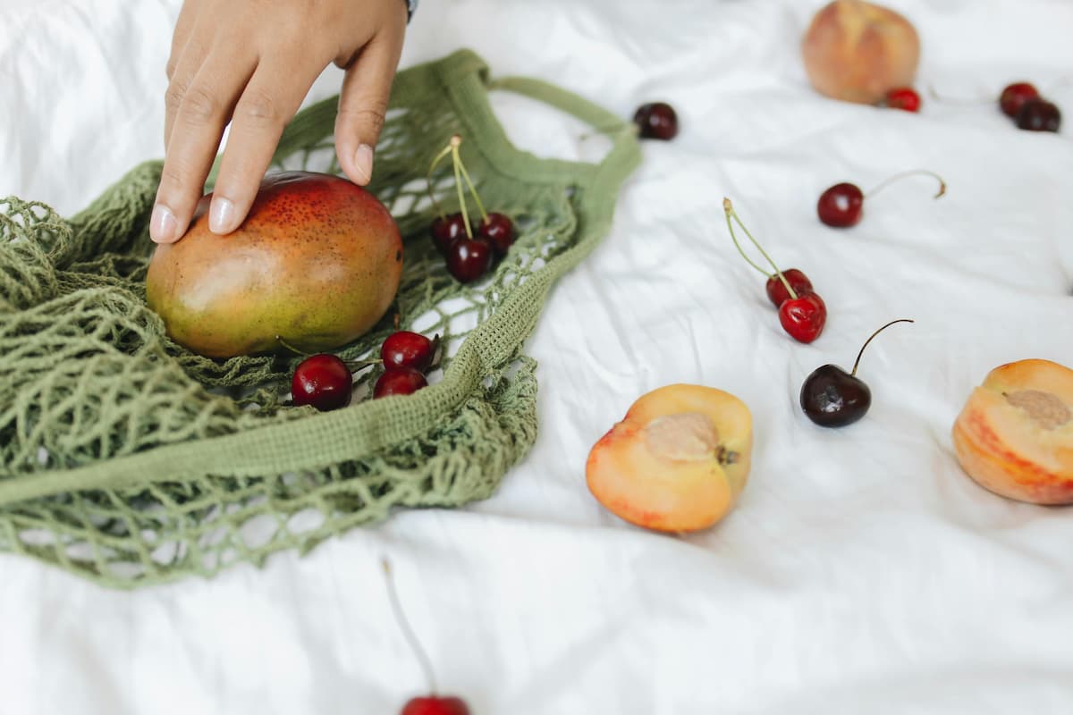 bag with cherries and a mango, open white peach in front