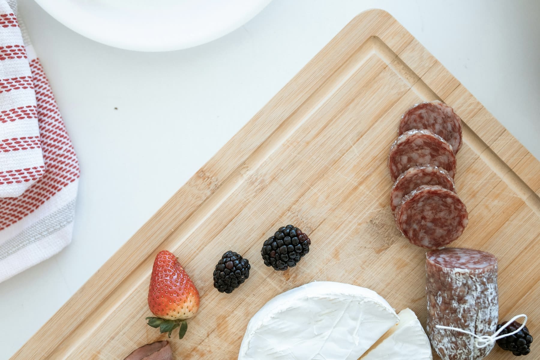 slices of genoa on a cutting board with berries and brie